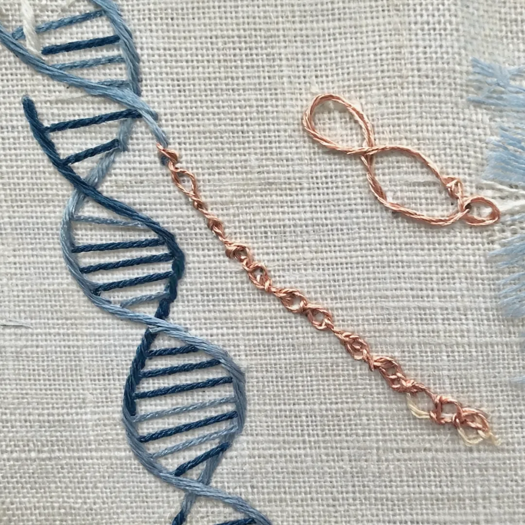 Close-up of a blue embroidered helix beside a copper chain stitched on linen canvas