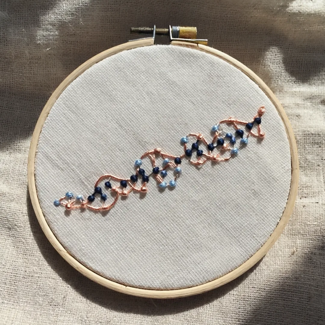Embroidered copper and navy helix with small beads on linen in a wooden hoop